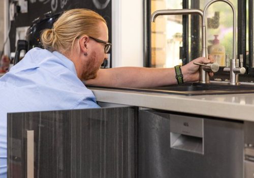 Professional plumber inspecting modern kitchen sink with copper tap fixture